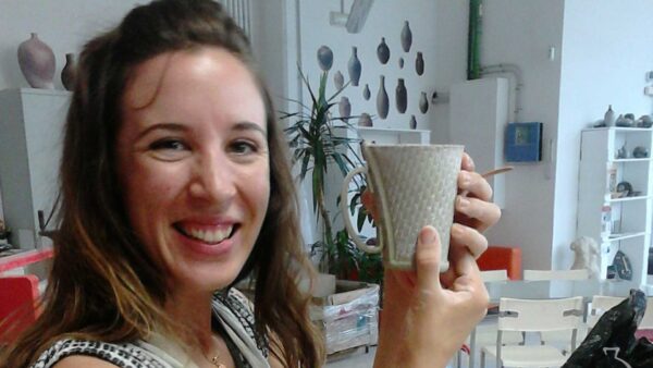 Una mujer sonriente sostiene una taza que ha elaborado en un taller de cerámica para principiantes