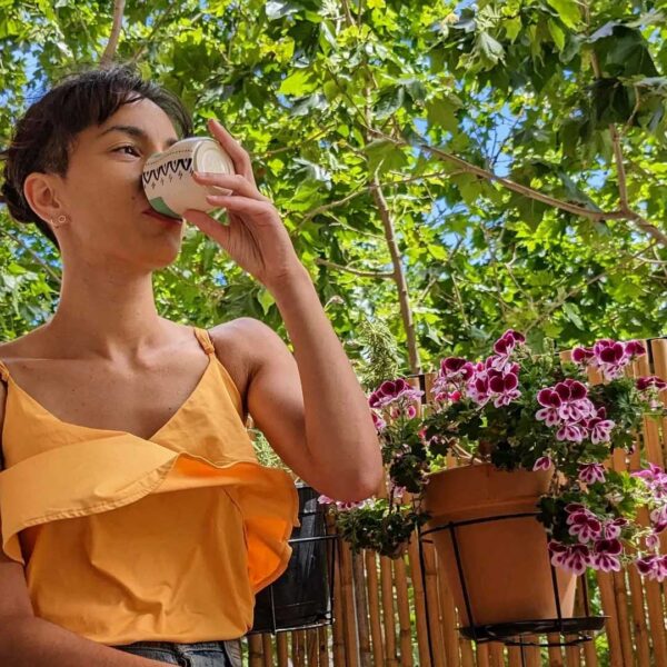 Mujer con blusa naranja bebiendo de una taza de barro artesanal